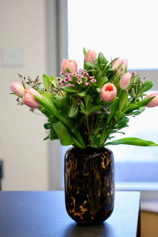 Bouquet of pink tulips and greenery in a tortoiseshell vase on a table.