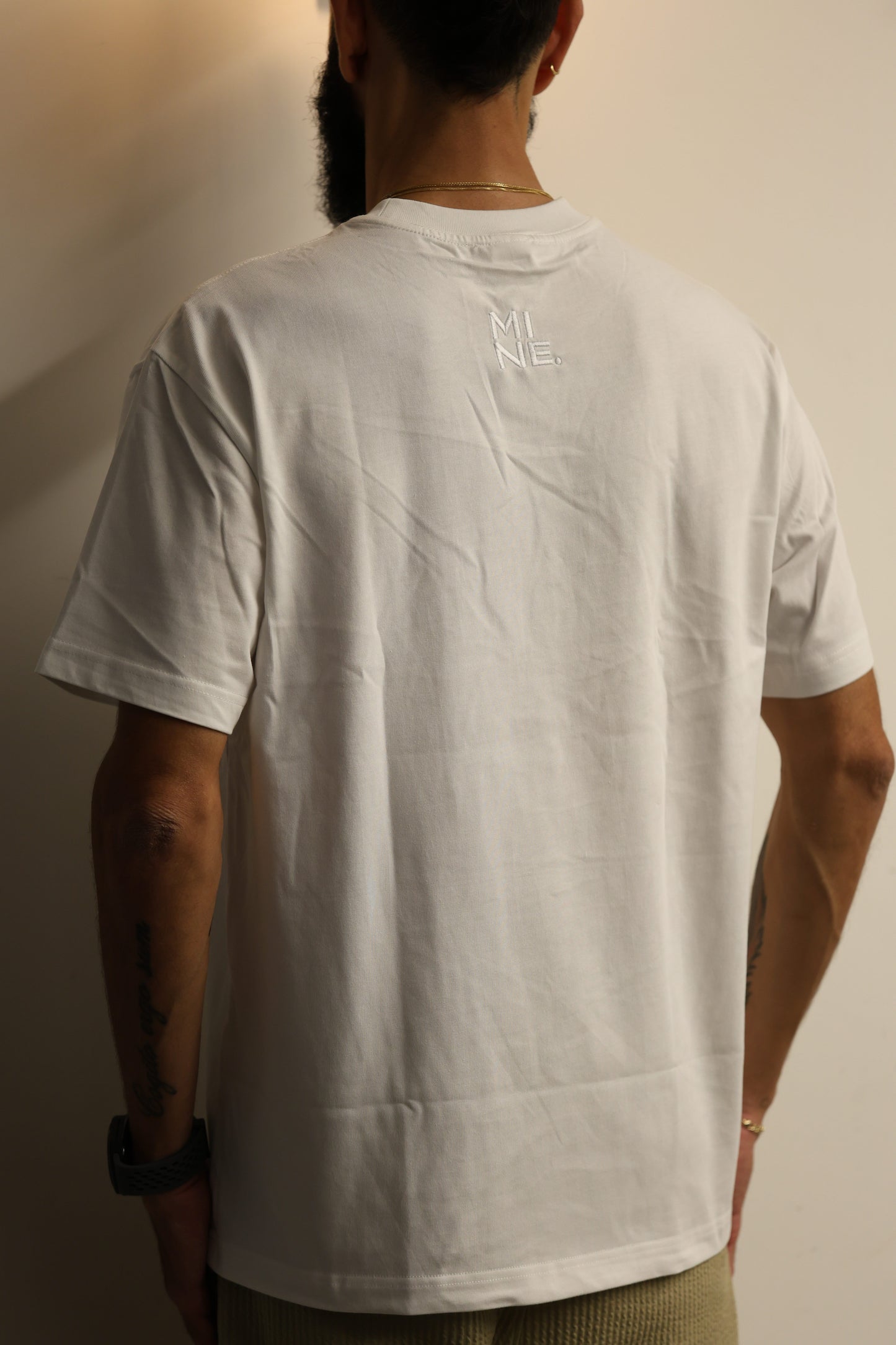 Person wearing a white t-shirt with a brand logo on a neutral background