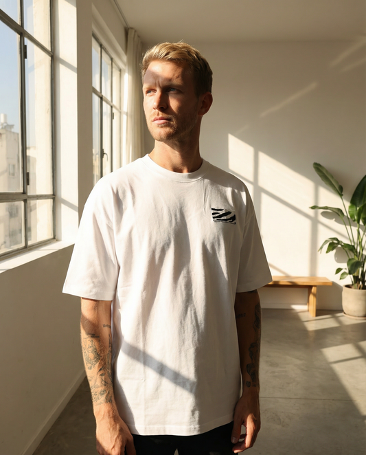 Man wearing a white t-shirt with a small design in a sunlit room