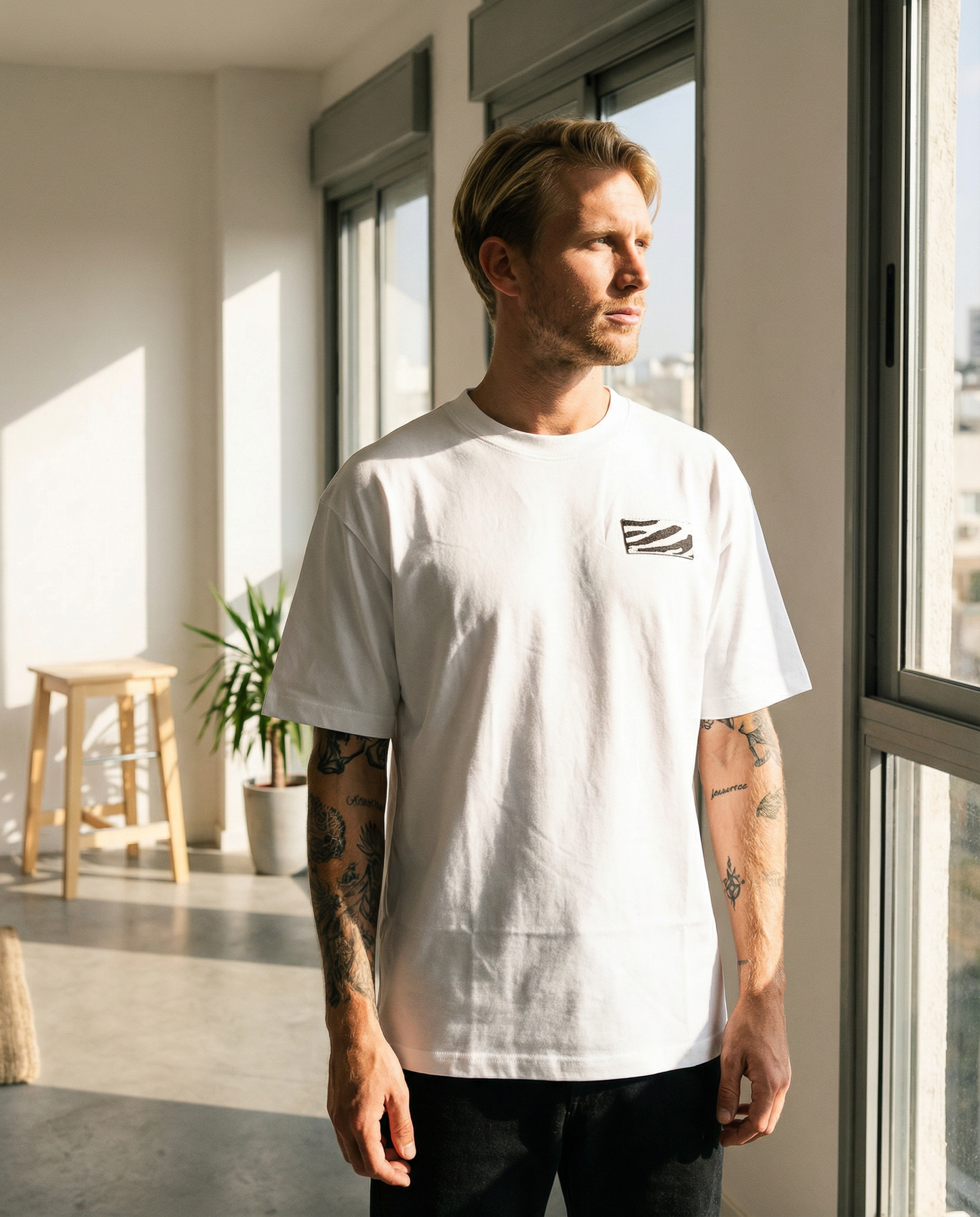 Man wearing a white t-shirt with a small graphic design, standing in a modern indoor setting.