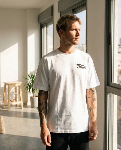 Man wearing a white t-shirt with a small graphic design, standing in a modern indoor setting.