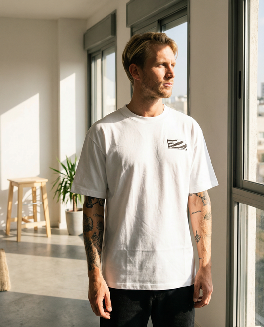 Man wearing a white t-shirt with a small graphic design, standing in a modern indoor setting.