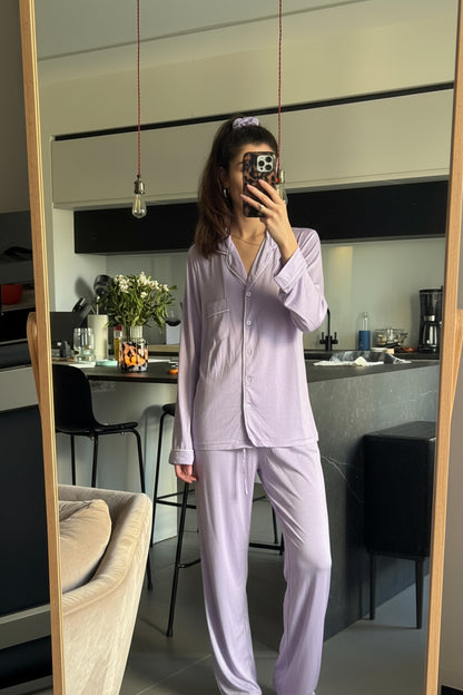 Person wearing a light purple pajama set taking a mirror selfie in a kitchen.