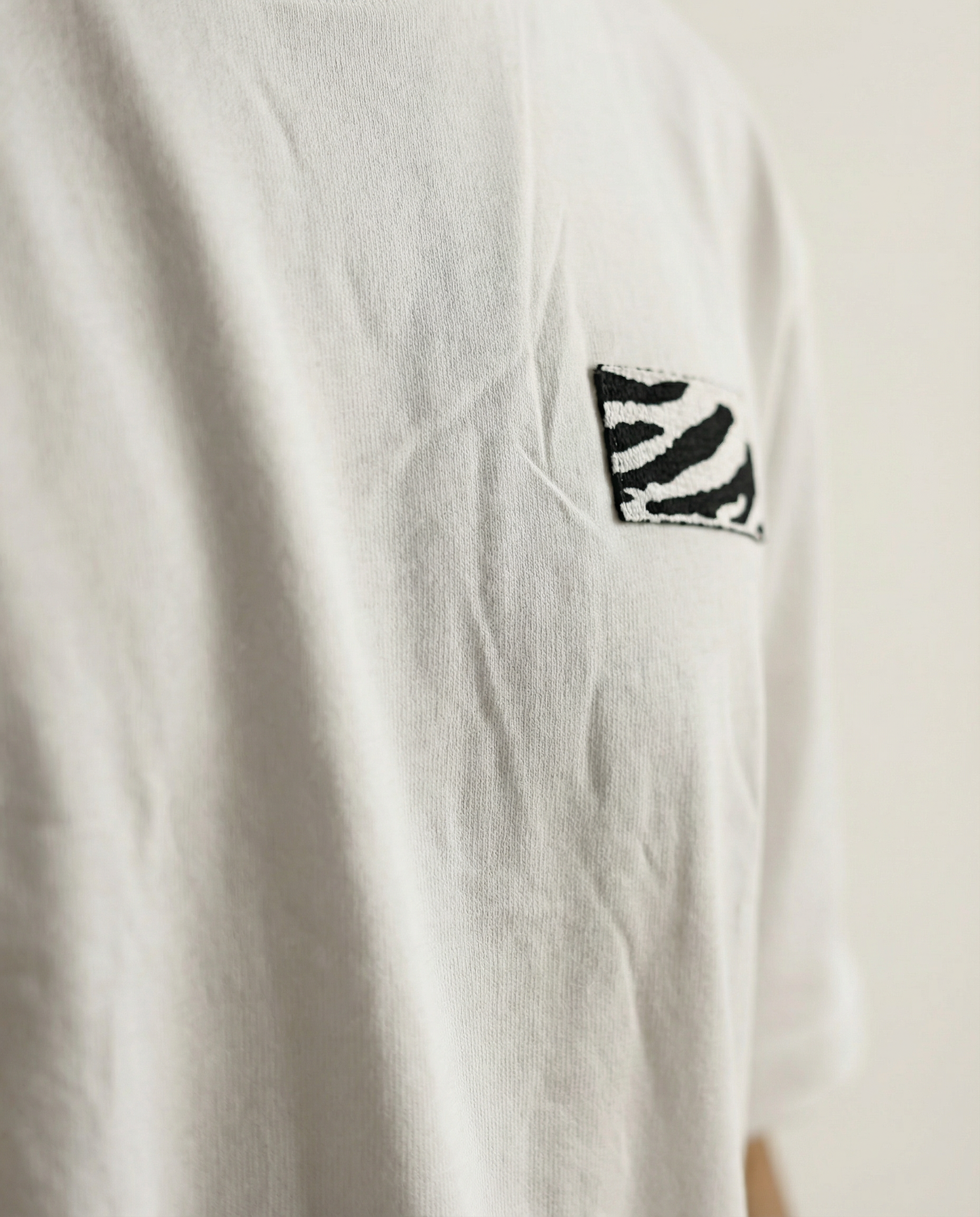 White t-shirt with a black and white zebra pattern on the chest against a beige background