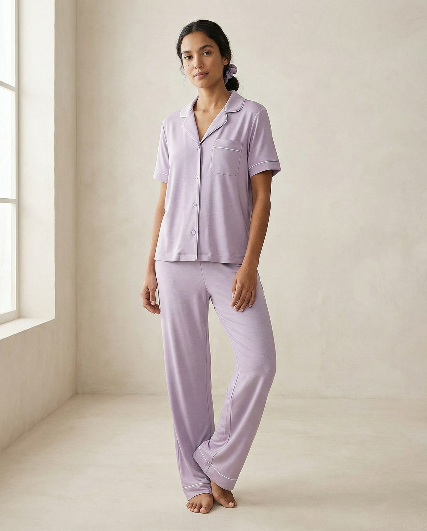 Woman wearing lavender pajamas standing in a bright room with a window.