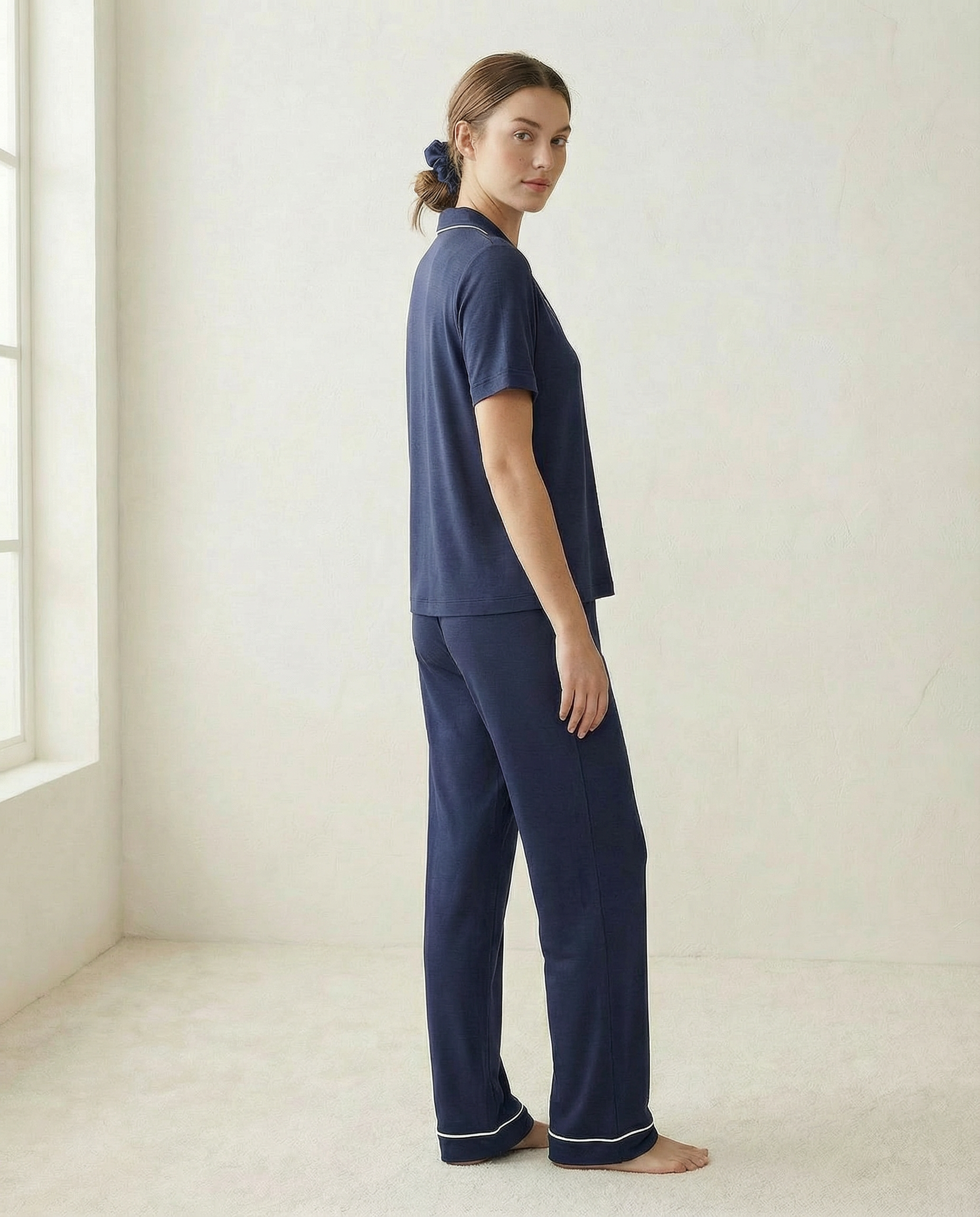 Woman wearing navy blue pajamas standing in a minimalistic room with a window.