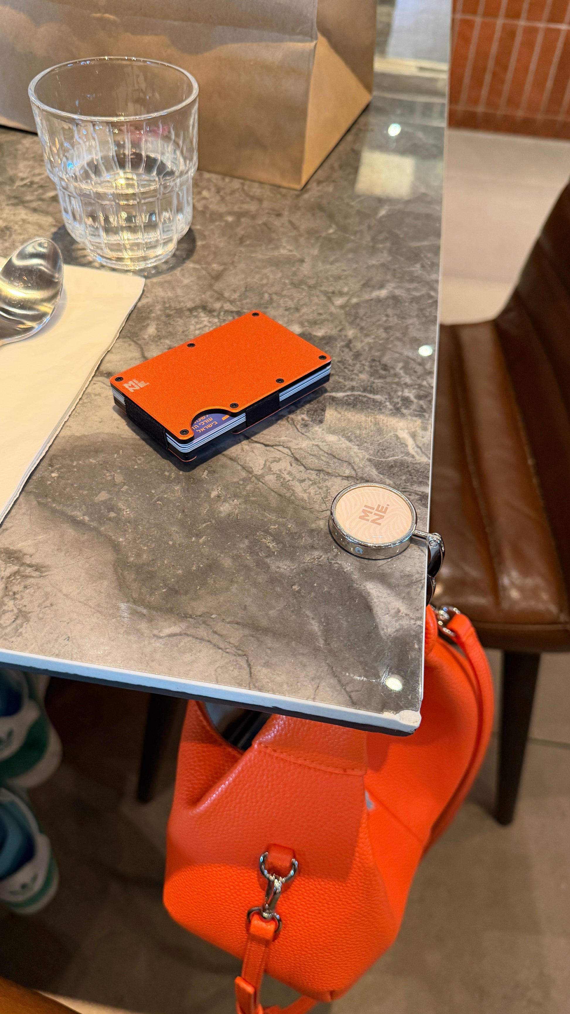 Orange wallet on a marble surface with a glass of water and a chair in the background.